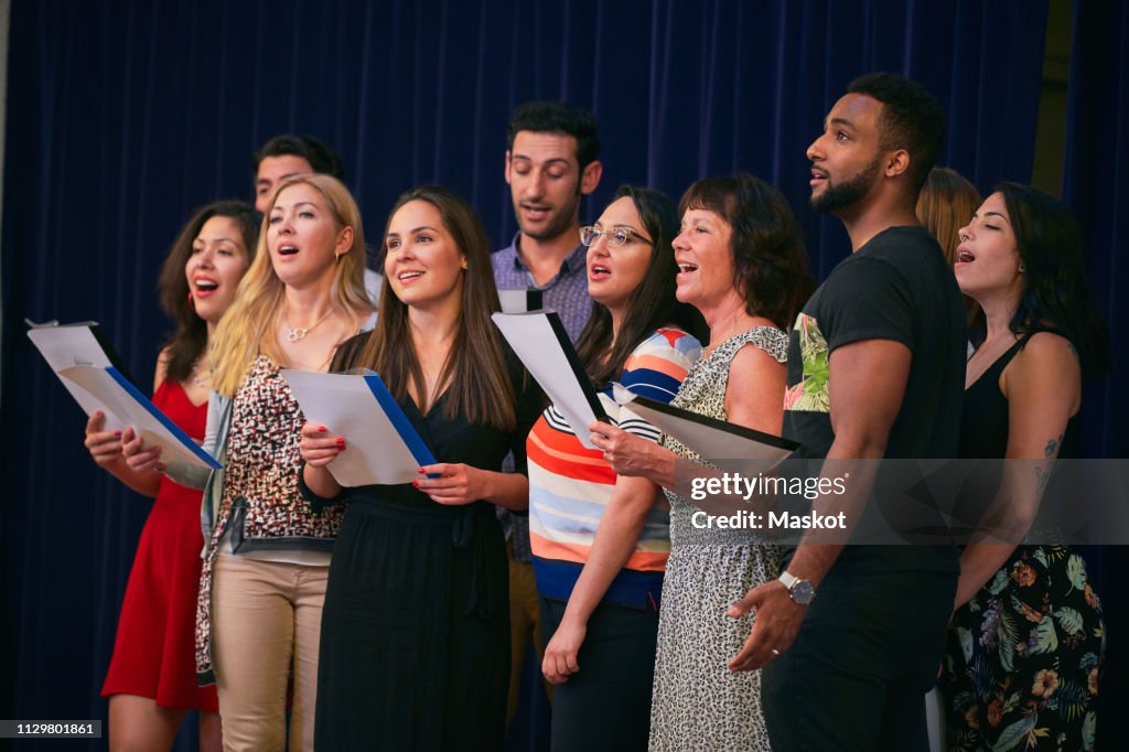 Male and female friends holding music sheets rehearsing on stage