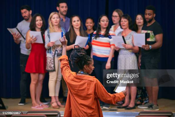young female conductor directing choir on stage in auditorium - dirigent stock-fotos und bilder