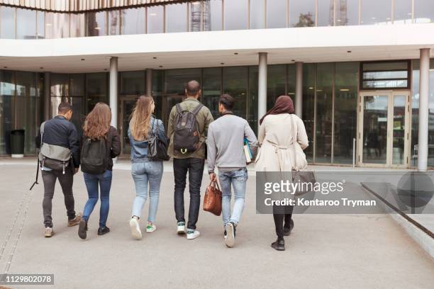 rear view of multi-ethnic students walking against building in high school campus - hijab woman from behind stock pictures, royalty-free photos & images