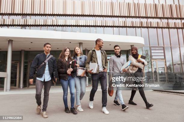 full length of multi-ethnic university students walking against building in campus - universitetsstudent bildbanksfoton och bilder