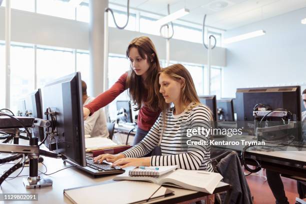 woman assisting friend while explaining over computer at library in university - doing a favor - fotografias e filmes do acervo