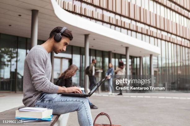 young student listening music while using laptop at university campus - male college student stock pictures, royalty-free photos & images