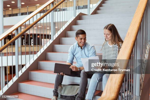 smiling friends discussing over documents while sitting on steps in university - 2 steps stock-fotos und bilder