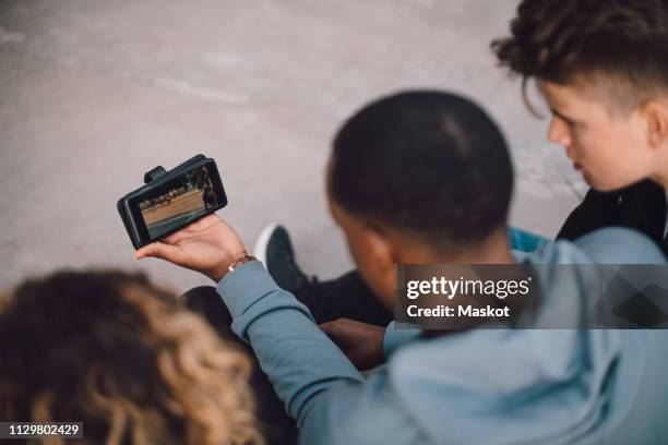 high angle view of male and female friends watching movie on smart phone - smartphone video stock pictures, royalty-free photos & images