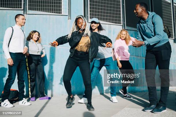 smiling friends looking at teenage girl dancing on sidewalk in city - oficios de eventos fotografías e imágenes de stock