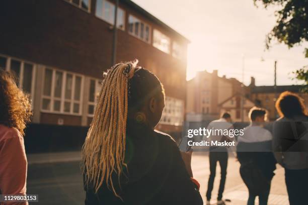 rear view of teenage girl text messaging on smart phone while walking with friends in city - rear view girl stockfoto's en -beelden