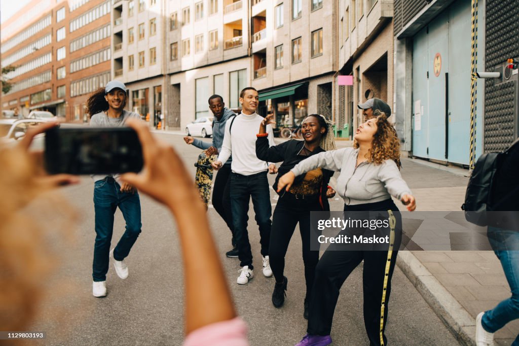 Woman photographing friends dancing on street in city