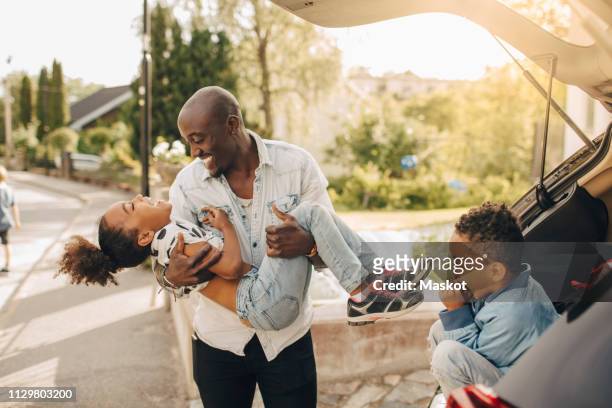boy looking at cheerful father carrying daughter by electric car on driveway - car on driveway bildbanksfoton och bilder