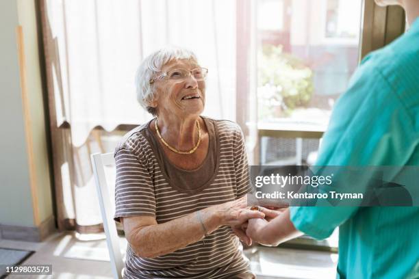 smiling senior woman holding hands of healthcare worker at nursing home - respect stockfoto's en -beelden