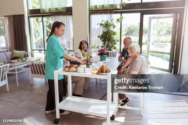 female caretaker serving breakfast to senior people in nursing home - serving cart stock pictures, royalty-free photos & images