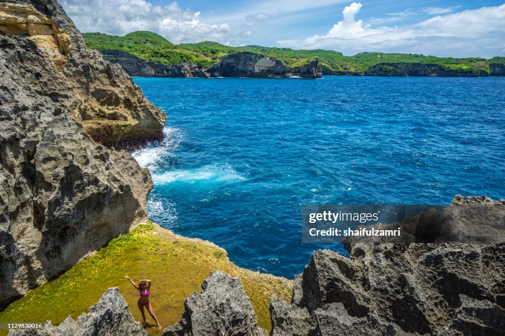 Tourist pose at Angel's Billabong, the natural pool on the island of Nusa Penida, Klingung regency, Bali, Indonesia.