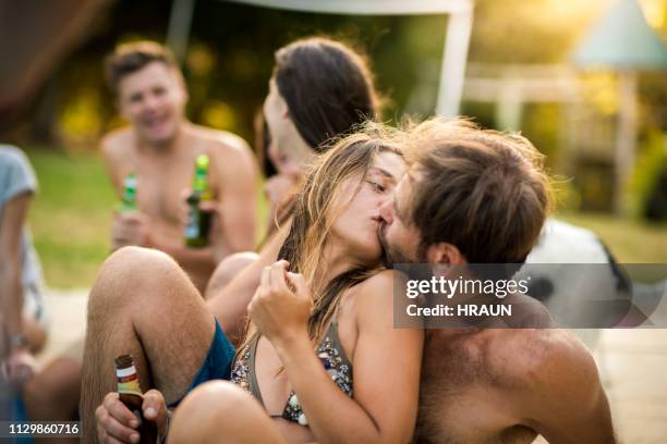 amantes de la pareja besándose mientras estaba sentado con sus amigos - beso en la boca fotografías e imágenes de stock