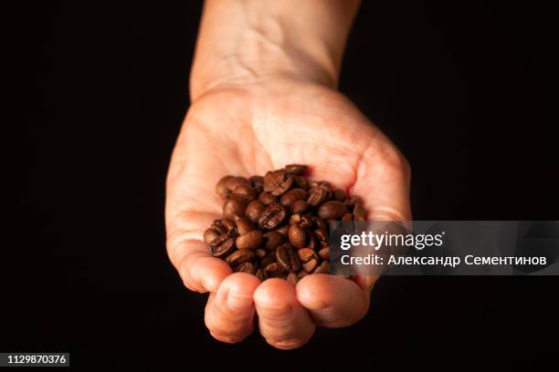 grain roasted black coffee in the palm on a black background. - hands full stock pictures, royalty-free photos & images