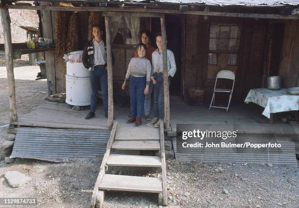 Four children on the porch of a log house, Pike County, Kentucky, US, 1967; on the side an old washing machine.