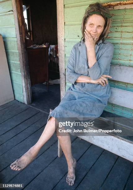 Woman sits barefoot on a bench on the porch of her house, Pike County, Kentucky, US, 1967.