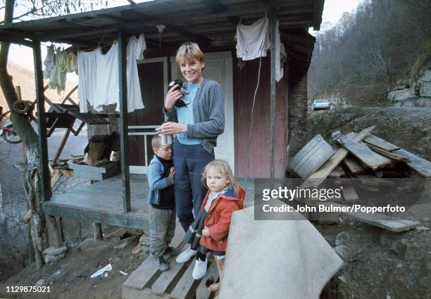 Woman, holding a kitty, outside a log house with her children, Pike County, Kentucky, US, 1967.