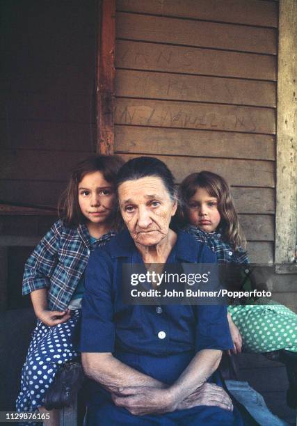 An elderly woman with two girls outside their log house, Pike County, Kentucky, US, 1967.