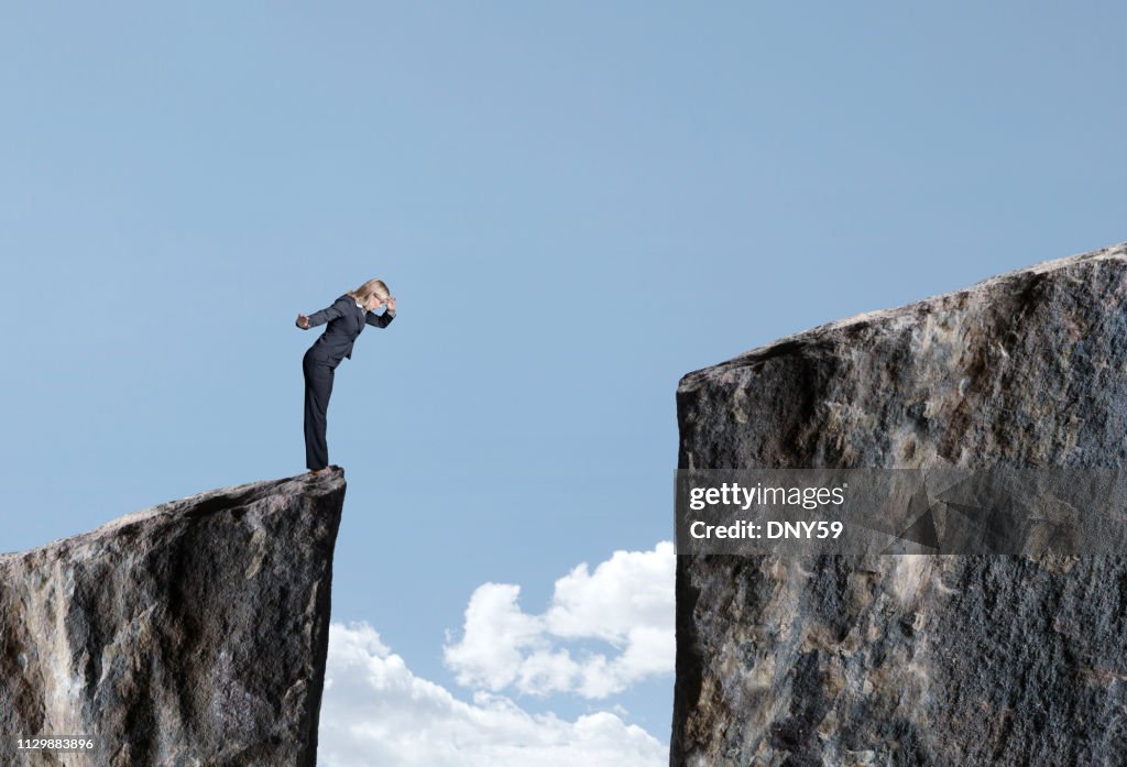 Businesswoman Looks Down At Large Gap Between Two Cliffs