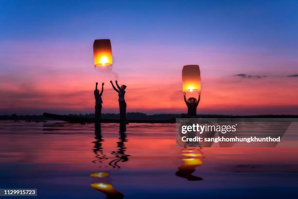 multi-generation family flying sky lanterns on mekong river at sunset, thailand - floating lanterns stock pictures, royalty-free photos & images