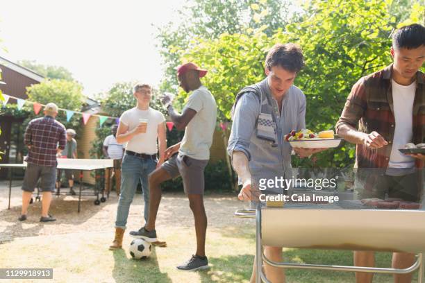male friends enjoying barbecue in sunny summer backyard - backyard football stock-fotos und bilder