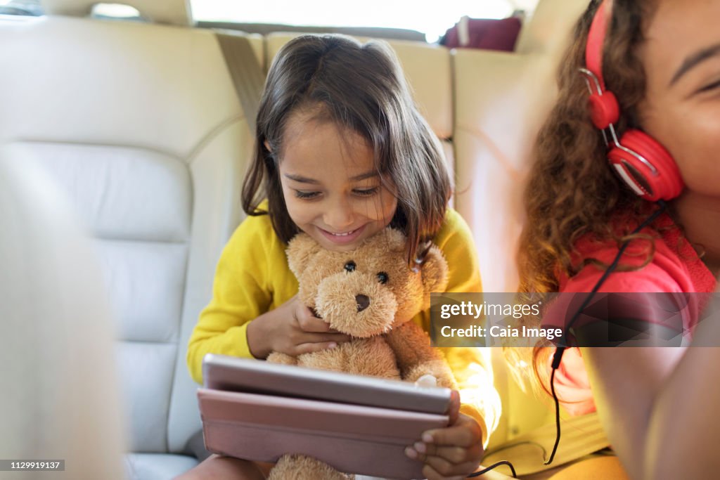 Cute girl with teddy bear using digital tablet in back seat of car