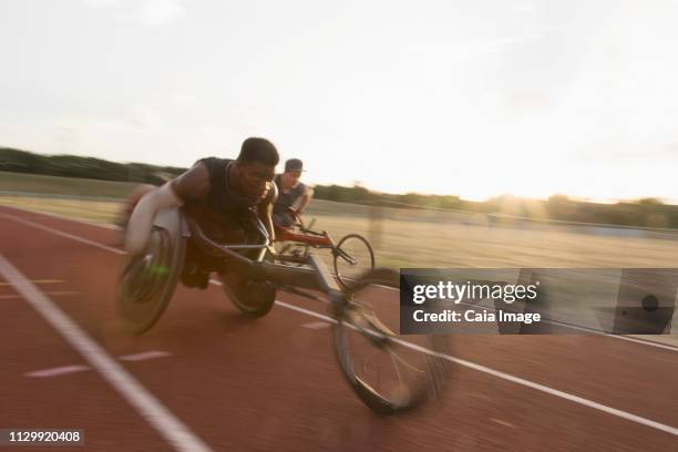 determined young male paraplegic athlete speeding along sports track in wheelchair race - carrera de sillas de ruedas fotografías e imágenes de stock