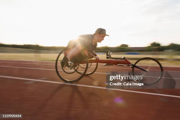 determined teenage boy paraplegic athlete speeding along sports track in wheelchair race - wheelchair athlete stock pictures, royalty-free photos & images