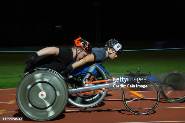 paraplegic athletes speeding along sports track during wheelchair race at night - wheelchair race stock pictures, royalty-free photos & images