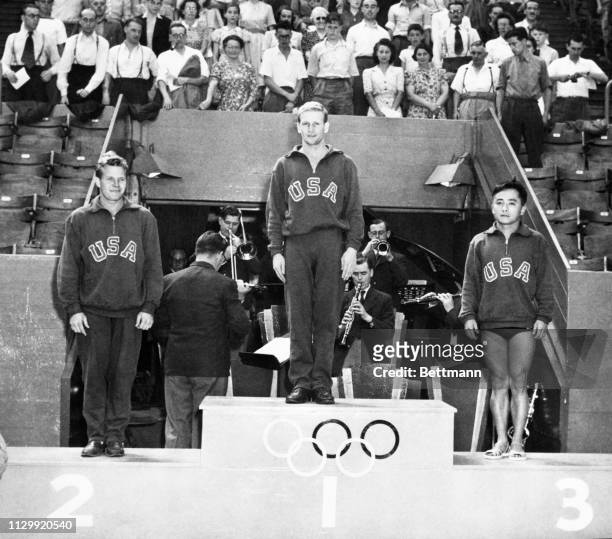 Bruce Harlan, of Ohio State, winner of the Olympic Men's Springboard diving title, stands at Rostrum at Empire Pool, flanked by teammates who came in...