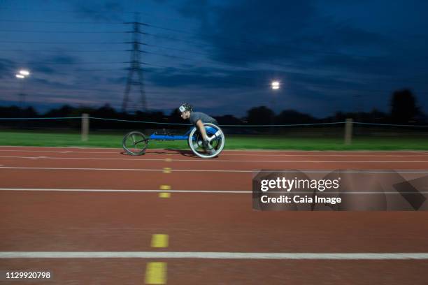 young female paraplegic athlete speeding along sports track in wheelchair race at night - paraplegic race stock pictures, royalty-free photos & images