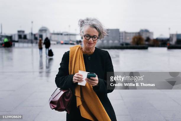 businesswoman smiling while texting on her lunch break - business walking stock-fotos und bilder