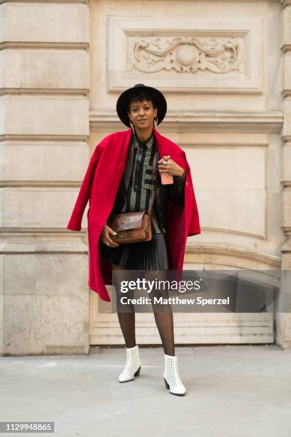 Guest is seen on the street wearing red coat, black/grey dress, black hat and brown leather bag with white shoes during London Fashion Week February...