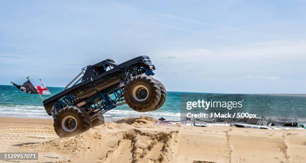 monster truck driving over car wrecks on sandy coastal beach - monster trucks stock pictures, royalty-free photos & images