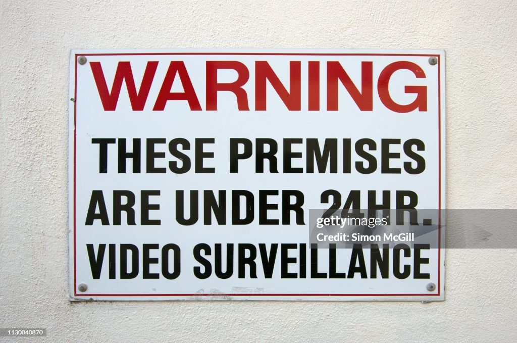 'Warning: These premises are under 24 hour video surveillance' sign on a building exterior wall