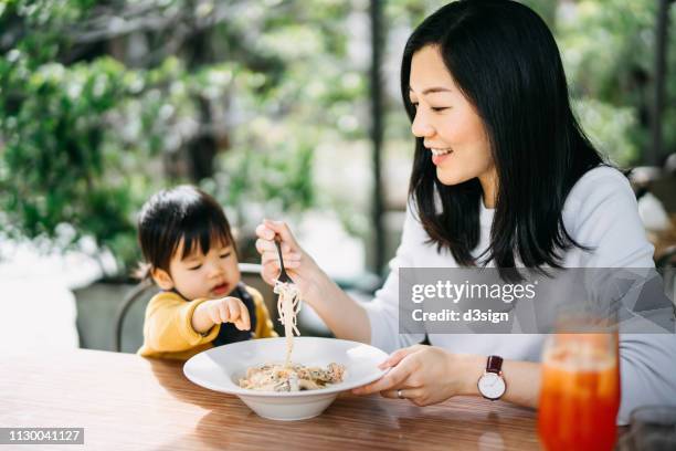 young mother and adorable toddler girl having meal joyfully in an outdoor cafe - asian baby eating fotografías e imágenes de stock