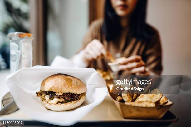 young woman sitting by the window eating burger with french fries with friends in a restaurant - sweet potato fries stock pictures, royalty-free photos & images