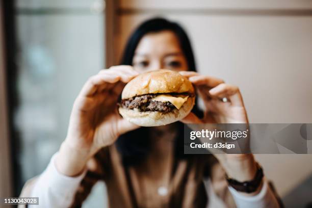 young woman holding a burger in front of her face and ready to bite into it - face covered stock pictures, royalty-free photos & images