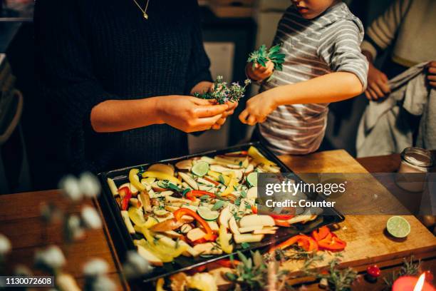 young boy sprinkling fresh herbs on vegetable dish - assado prato principal - fotografias e filmes do acervo