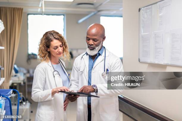 mehrethnische ärzte diskutieren über dokumente - krankenblatt stock-fotos und bilder