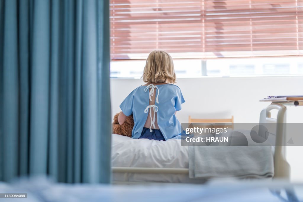 Rear view of sick girl sitting on hospital bed
