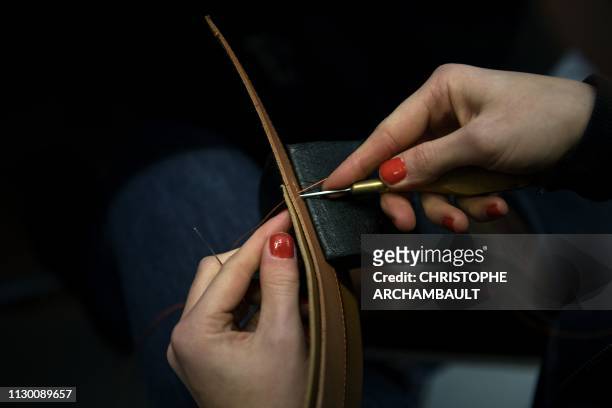Craftsman stitches pieces of leather as part of a saddle at the French luxury brand Hermes' saddlery in Paris on March 11, 2019. - Since 1880, Hermes...