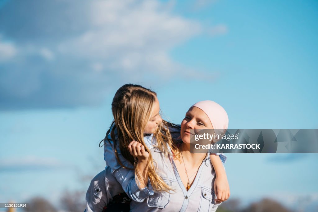 A woman with cancer is next to her daughter. A girl is hugging a woman happy