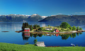 Hardangerfjord in south western Norway in the summer. A red, Norwegian house situated on a small island in the fjord. In the distance the Folgefonna glacier.