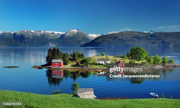 hardangerfjord in south western norway in the summer. a red, norwegian house situated on a small island in the fjord. in the distance the folgefonna glacier. - boat scandinavia stock pictures, royalty-free photos & images
