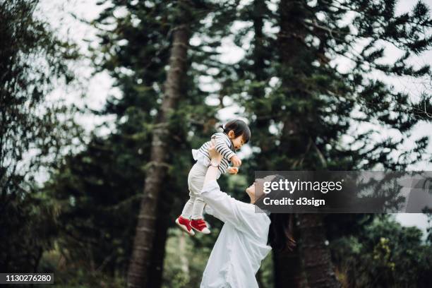 joyful mother enjoying happy family time with cute toddler girl and lifting her in the air in nature park - baby nature stock pictures, royalty-free photos & images