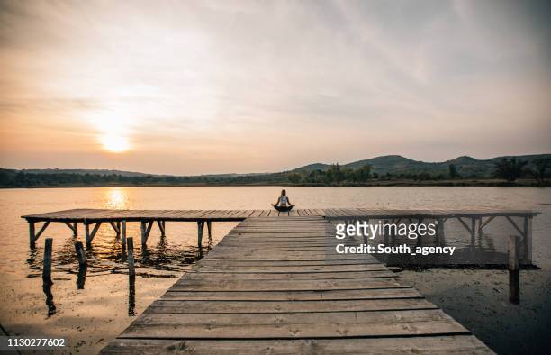 woman meditating by a beautiful lake - tranquil scene stock pictures, royalty-free photos & images