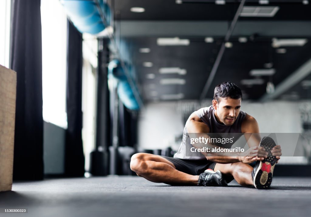 Young man doing leg stretches in the gym