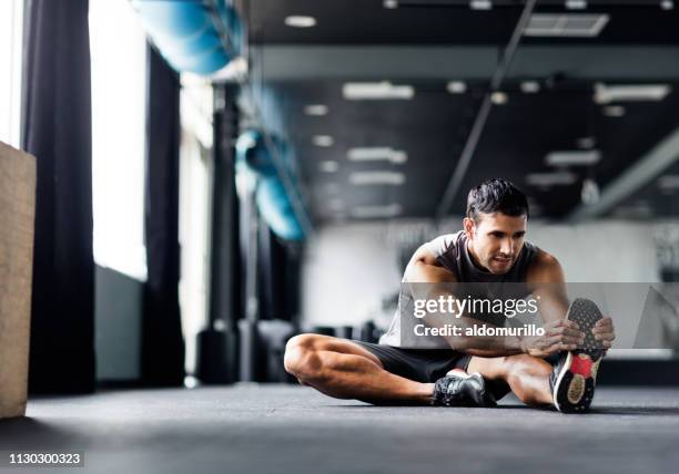 young man doing leg stretches in the gym - cooling down stock pictures, royalty-free photos & images