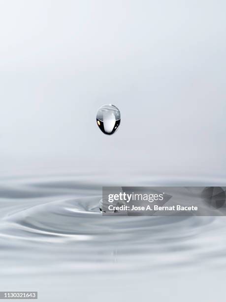 group of drops on line suspended in the air, falling down on a water surface that forms figures and abstract forms, on a white background. - tropfen aufprall stock-fotos und bilder