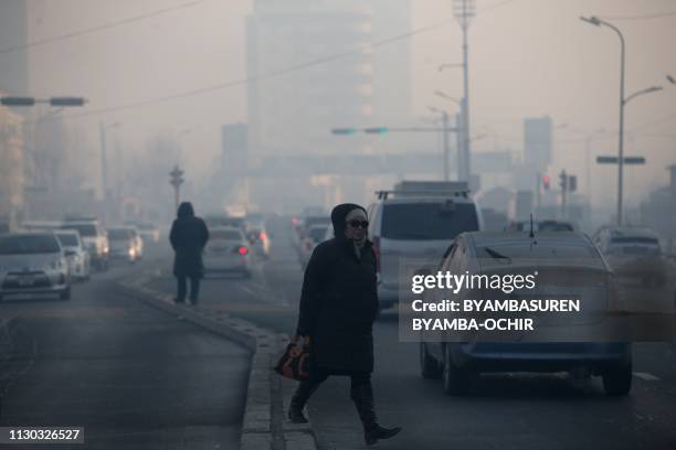 This picture taken on February 14, 2019 shows a woman walking across a road on a polluted day in Ulaanbaatar, the capital of Mongolia. - In the...